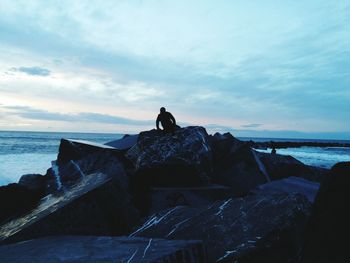 Man standing on rock by sea against sky