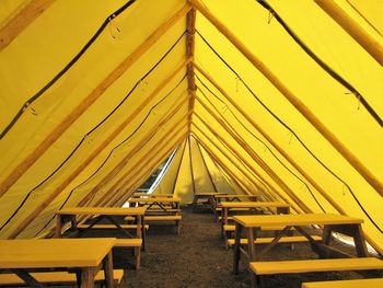 Picnic tables under long yellow tent supported by logs with 