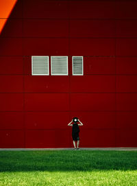 Full length of woman walking on field against red wall