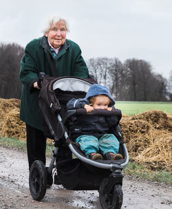 Portrait of senior woman pushing stroller with baby girl on road