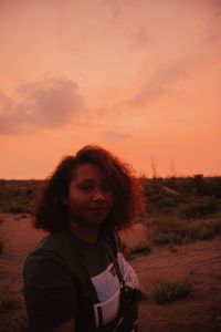 Portrait of young woman standing on field during sunset