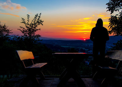 Rear view of silhouette man standing on chair at sunset