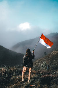 Woman standing with flag on field against mountains