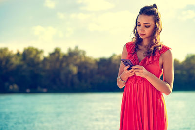 Young woman using phone while standing on shore