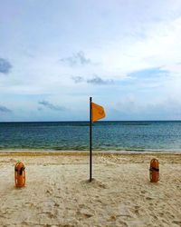 Orange flag waving at sandy beach against cloudy sky