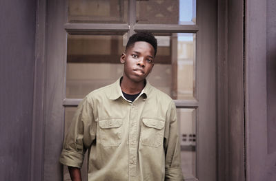 Portrait of young black skin man standing against wooden door.
