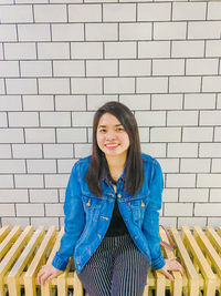 Portrait of a smiling young woman against brick wall