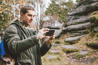 Man photographing by mobile phone while standing in forest