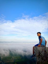 Teenage boy sitting on rock against landscape covered with fog