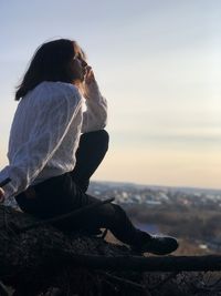 Woman sitting on rock looking at sea against sky