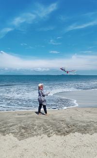 Rear view of woman standing at beach against sky