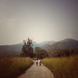 Rear view of people walking on road in field