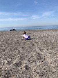 Rear view of woman sitting on beach against sky