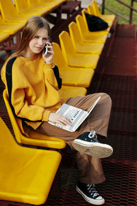 A pretty schoolgirl or student is sitting at the stadium during a break and talking on the phone