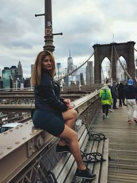 Portrait of woman sitting on brooklyn bridge against sky