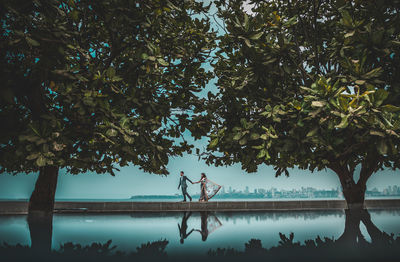 People standing by tree against sky