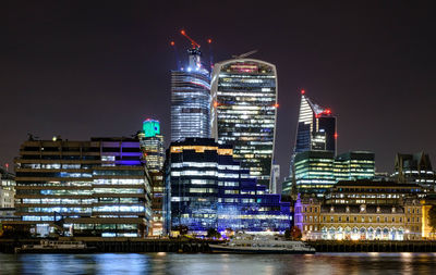 Illuminated buildings by river against sky at night