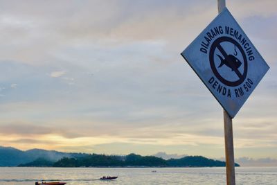 Close-up of road sign by sea against sky