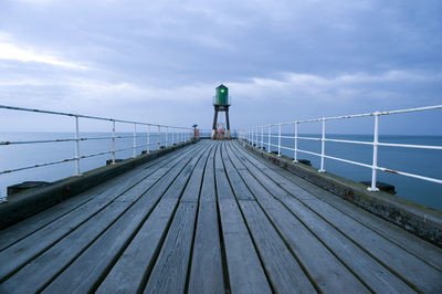 Lighthouse on wooden pier against cloudy sky