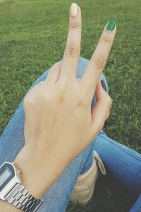 Low section of woman showing peace sign on grassy field