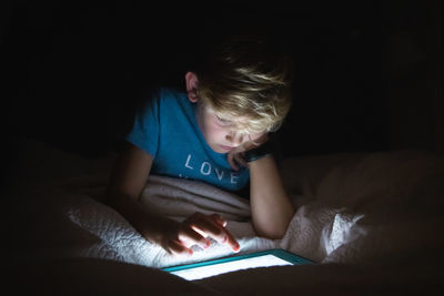Boy using digital tablet sitting on bed at home