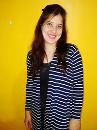 Portrait of smiling young woman against yellow wall