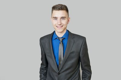 Portrait of young smiling businessman wearing suit while standing against gray background