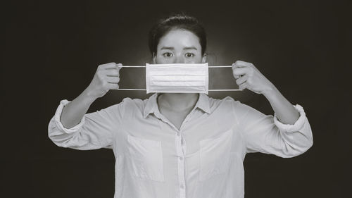 Portrait of young man holding mask against black background