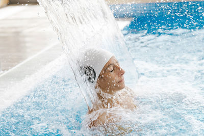 Young woman with swimming cap relaxing under a waterfall jet in a spa person