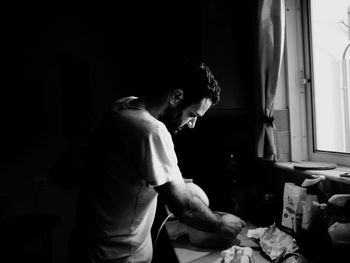 Side view of man using wire wisk on table at home