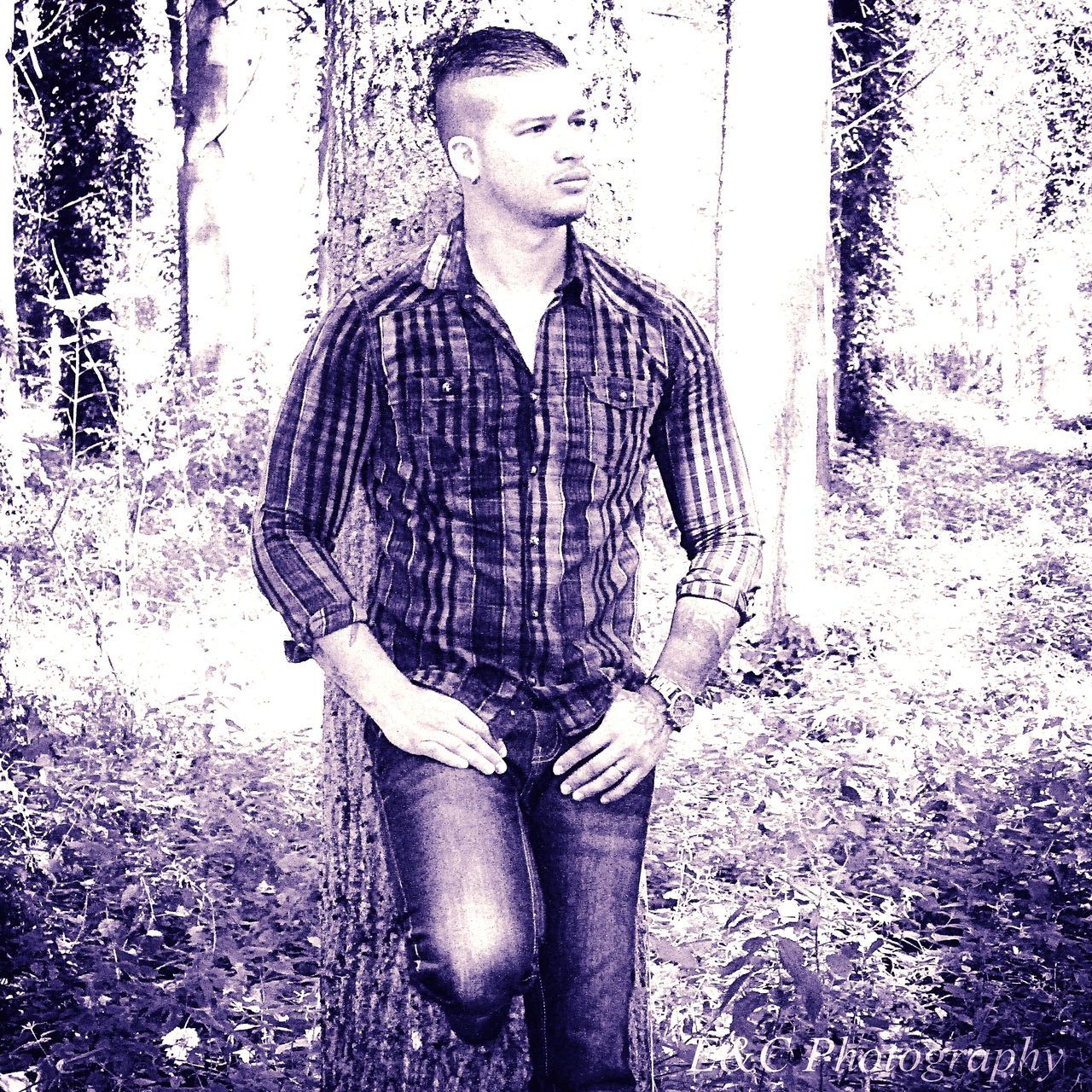 PORTRAIT OF YOUNG MAN STANDING ON TREE TRUNK IN FOREST