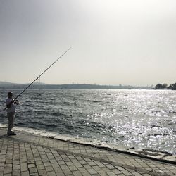 Man fishing at sea against clear sky