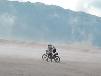 Man with motorcycle on dirt road against mountain