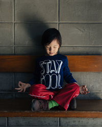 Front view of a cute boy doing yoga on a bench