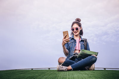 Young woman wearing sunglasses sitting against sky