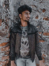 Portrait of young man looking away against wall