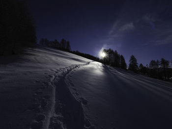 Road amidst snow covered land against sky at night