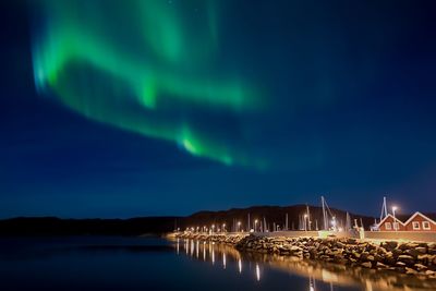 Illuminated pier by sea against sky at night