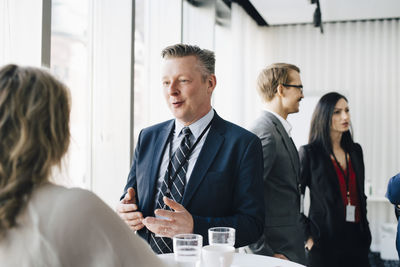 Male entrepreneur talking to colleague while coworker standing in background at workplace