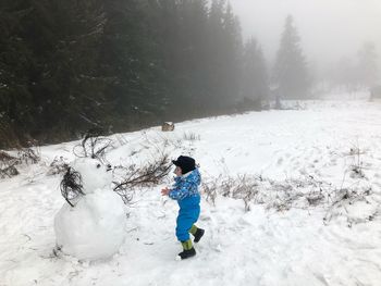 Full length of boy looking at snowman in winter