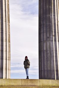 Woman standing amidst columns against sky