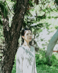 Young woman standing by tree trunk in forest