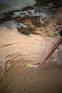 Cropped hand of woman picking plastic bottle from lake