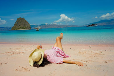 Rear view of woman sitting at beach against sky