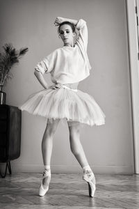 Charming ballerina poses showing her legs in the room in front of the mirror in pointes and tutu