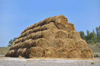 Hay bales on field against clear blue sky