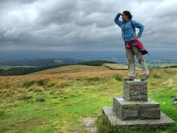 Woman standing on stone against cloudy sky