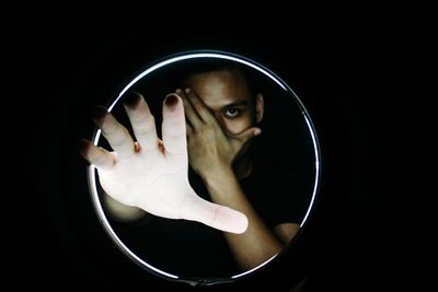 Close-up portrait of woman with hands against black background