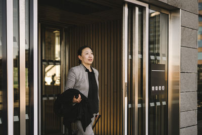 Confident female professional with luggage walking out from building