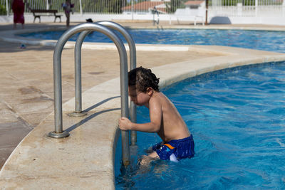 Rear view of shirtless boy swimming in pool